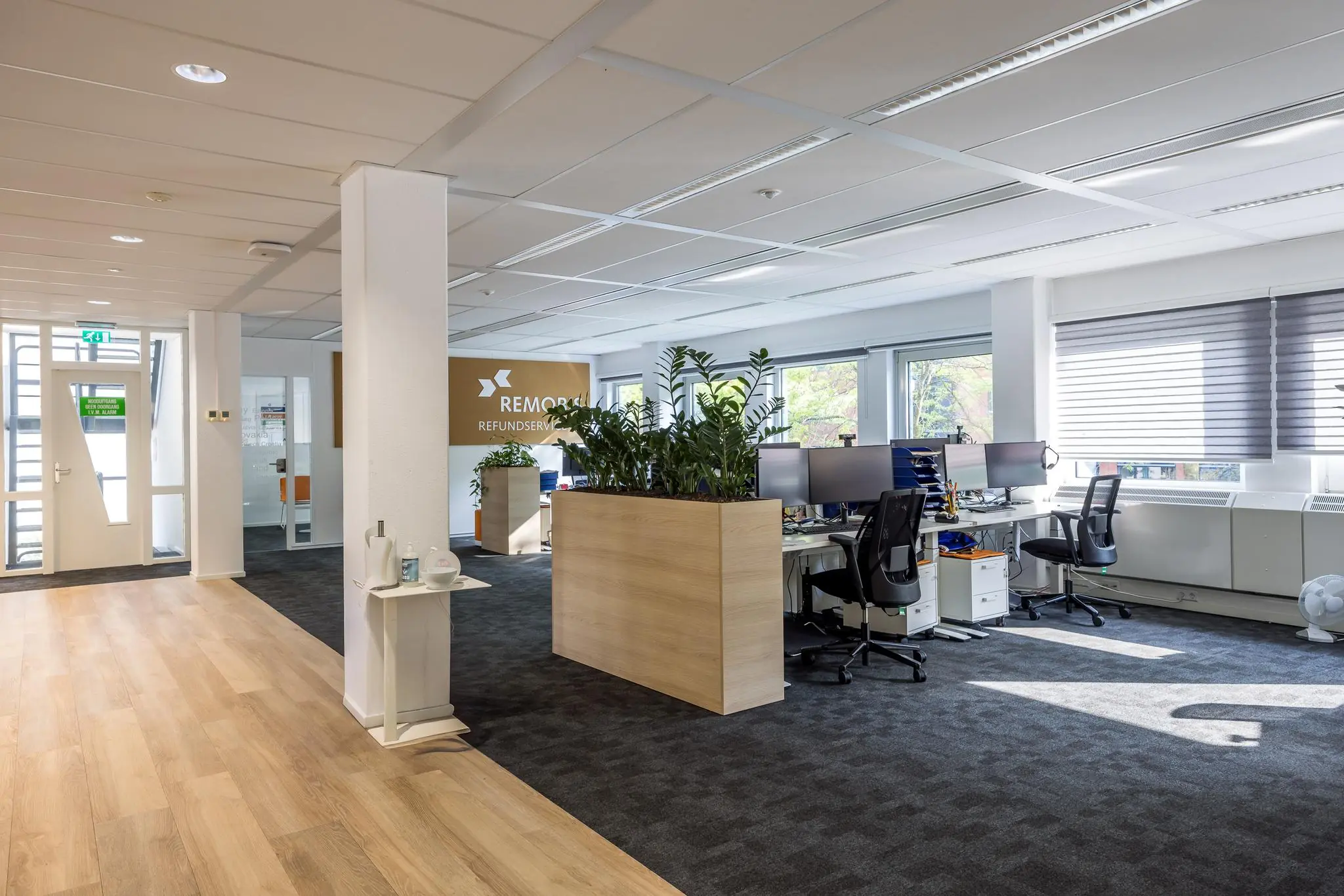 Modern kantoorinterieur van REMOR Refundservice met werkplekken, plantenbakken en veel natuurlijk licht.