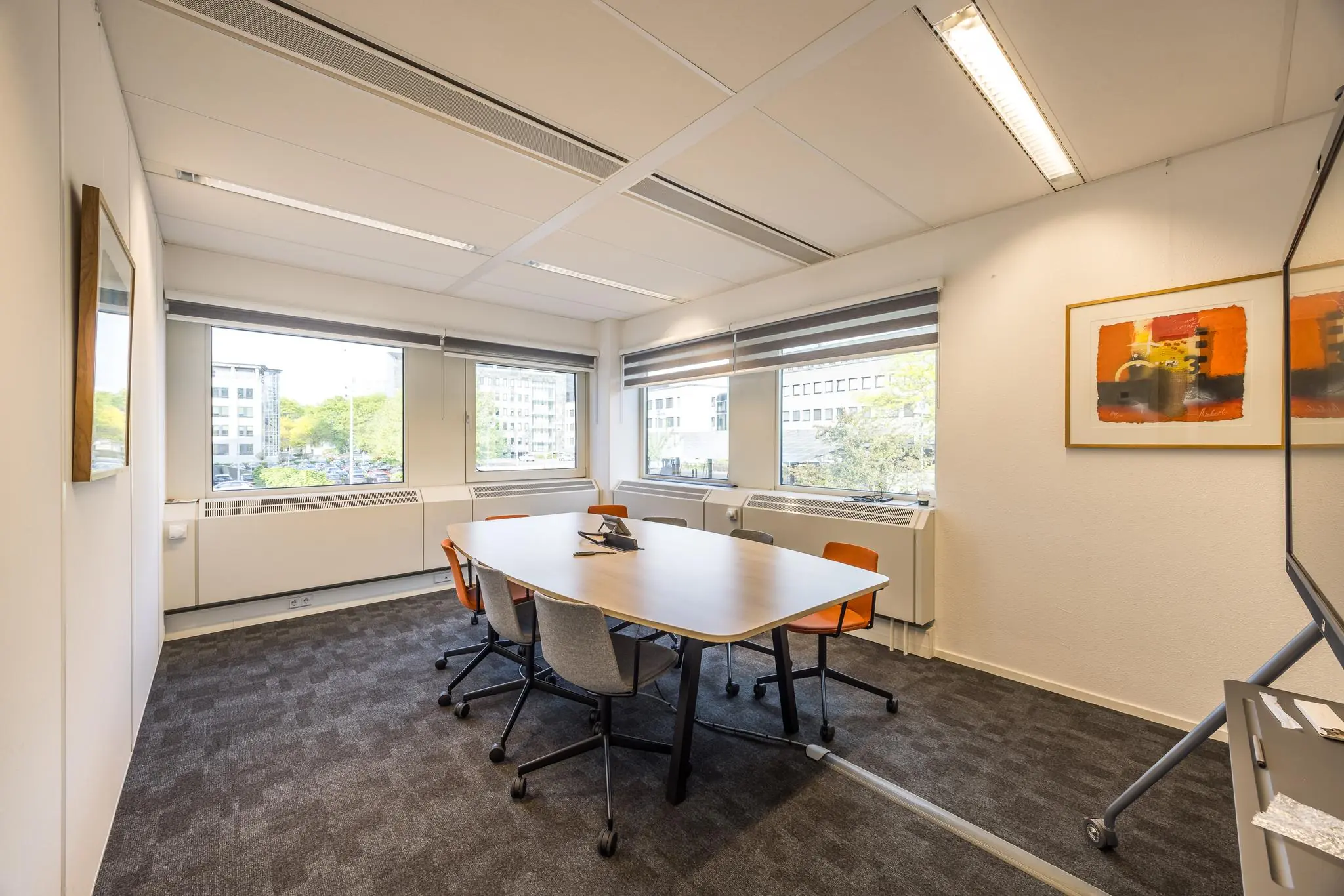 Vergaderruimte aan de Varrolaan met rechthoekige tafel, zes stoelen en grote ramen met uitzicht op kantoorpanden.