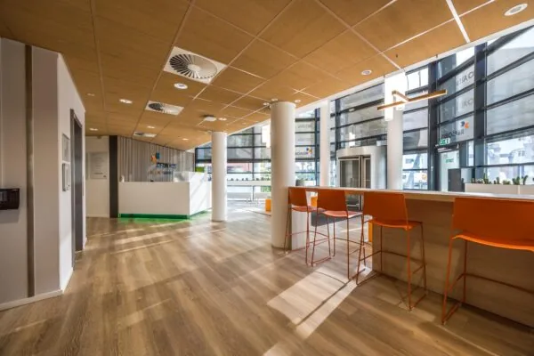 Moderne ontvangsthal van REMOBIS aan de Varrolaan met houten vloer, oranje stoelen en een witte balie.