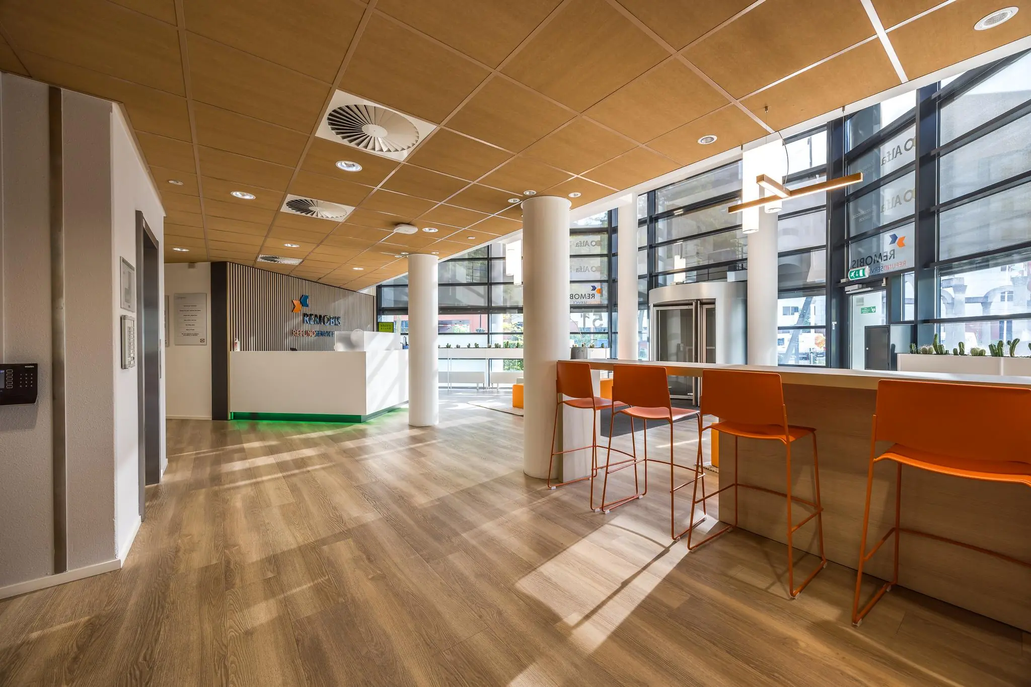 Moderne ontvangsthal van REMOBIS aan de Varrolaan met houten vloer, oranje stoelen en een witte balie.