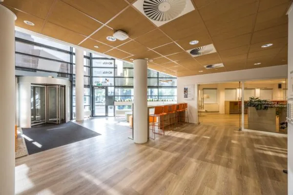 Moderne en lichte ontvangsthal aan de Varrolaan met glazen entreedeuren, zitgedeelte en oranje barkrukken.