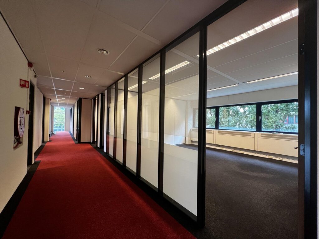 Gang met rood tapijt en glazen kantoormuren in een kantoorpand aan de Vreeswijksestraatweg.