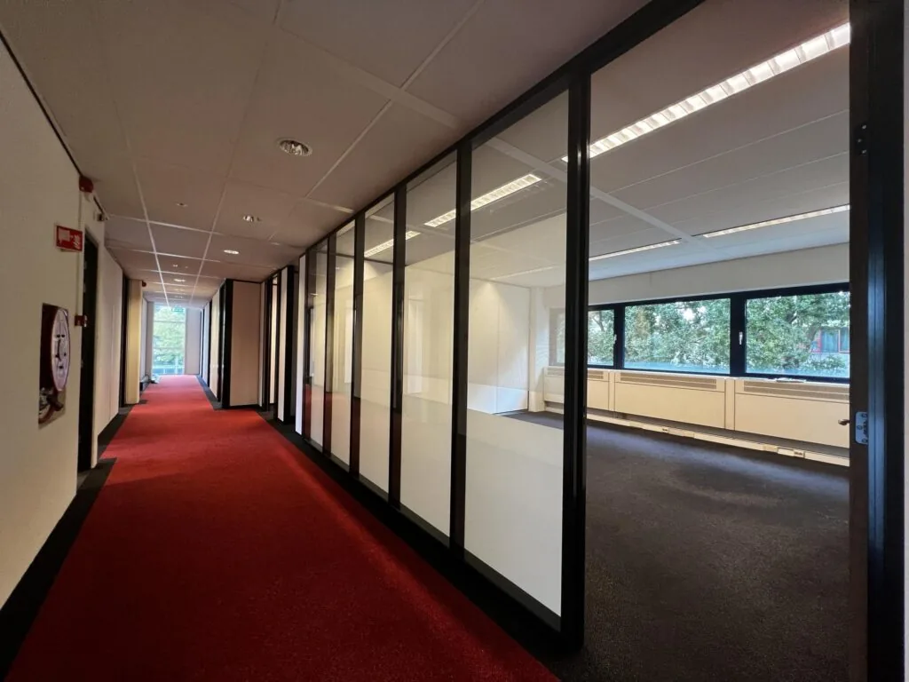 Gang met rood tapijt en glazen kantoormuren in een kantoorpand aan de Vreeswijksestraatweg.