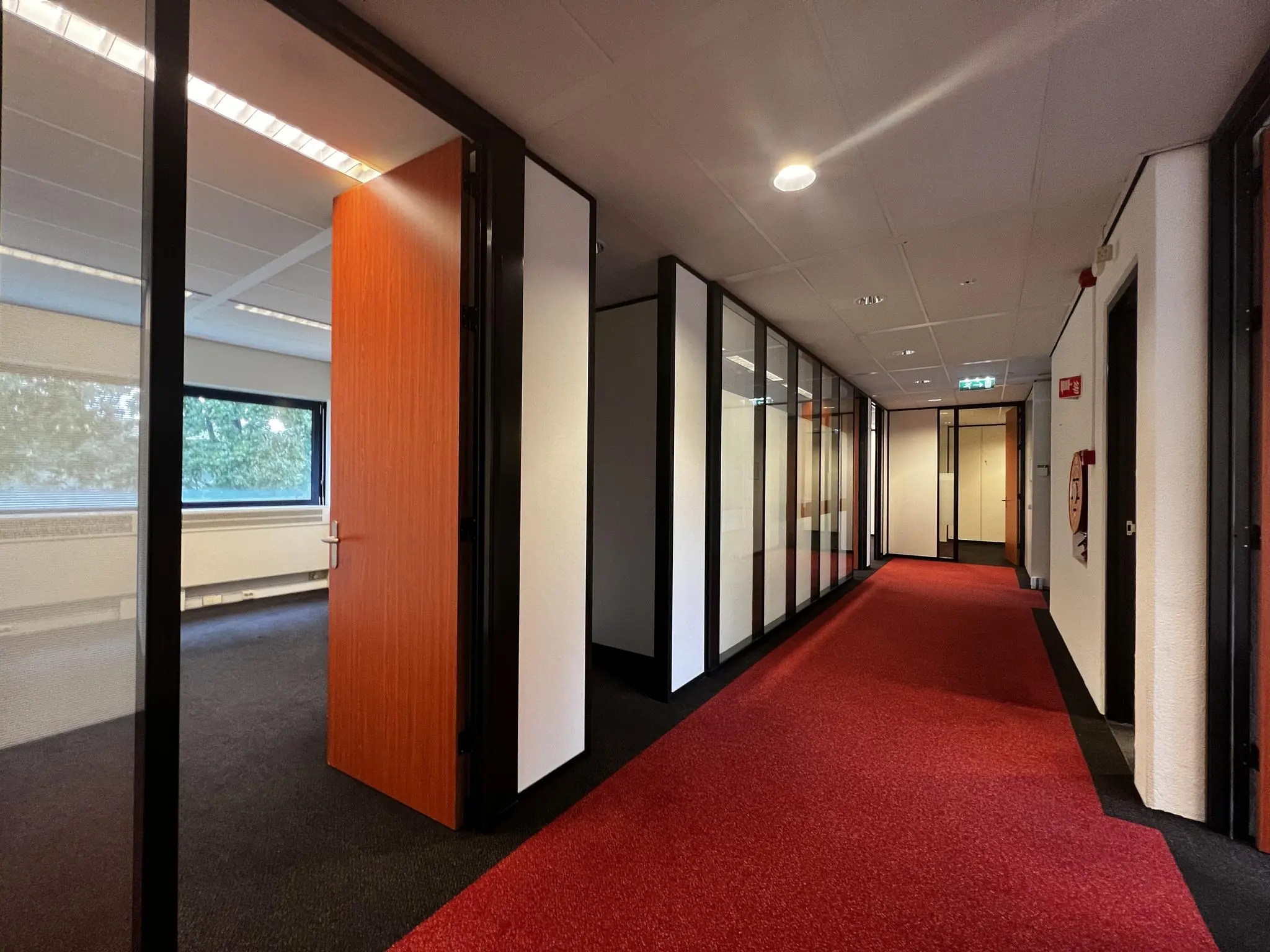 Kantoorhal aan de Vreeswijksestraatweg met rood tapijt, glazen wanden en een deels open deur naar een kantoorruimte.