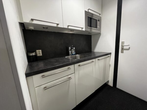 Kleine moderne kitchenette met witte kasten, een ingebouwde magnetron en een zwart aanrechtblad aan de Vreeswijksestraatweg.