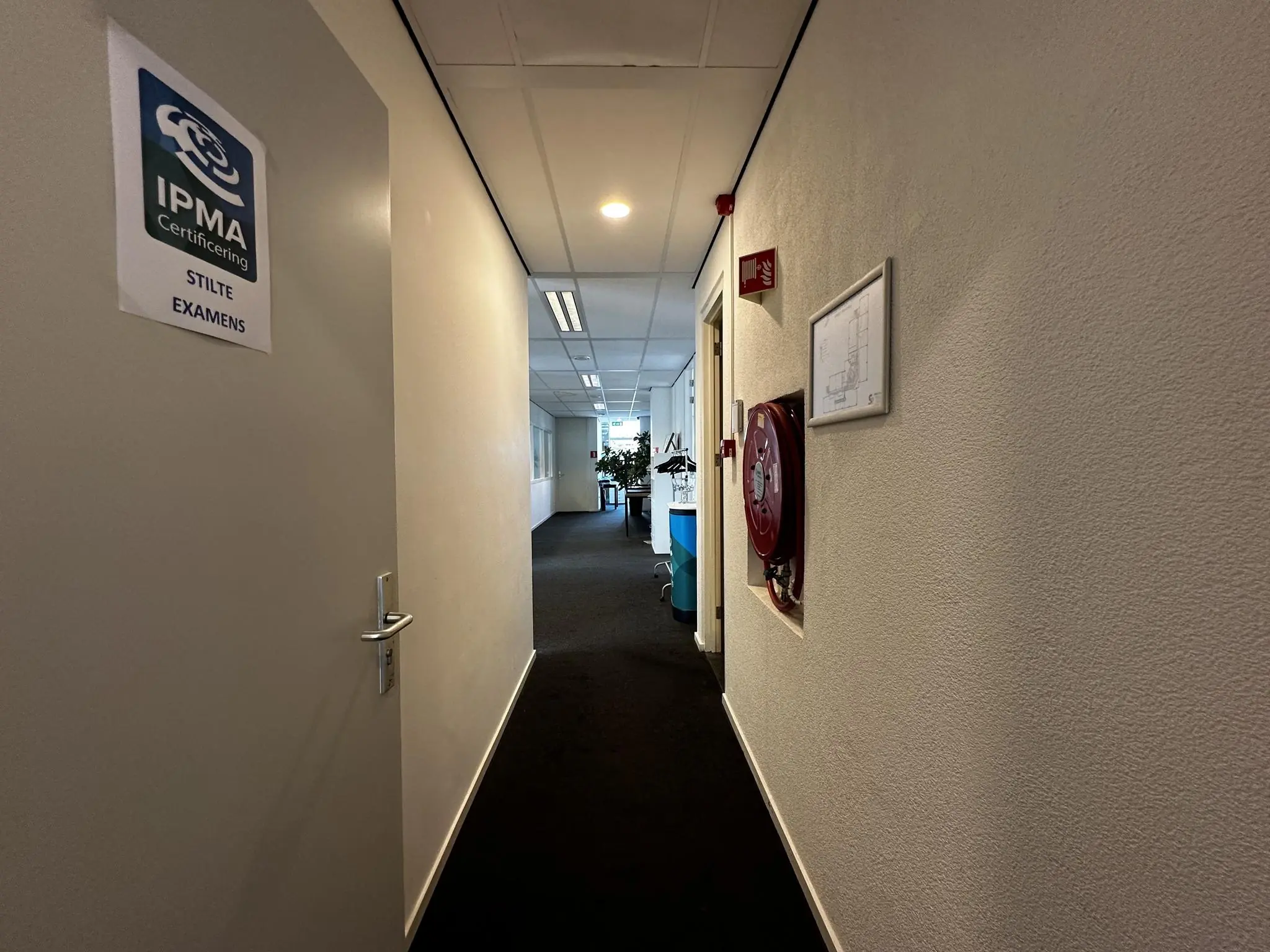 Gang van een kantoorpand aan de Vreeswijksestraatweg met een open deur naar een stilteruimte voor IPMA-examens.