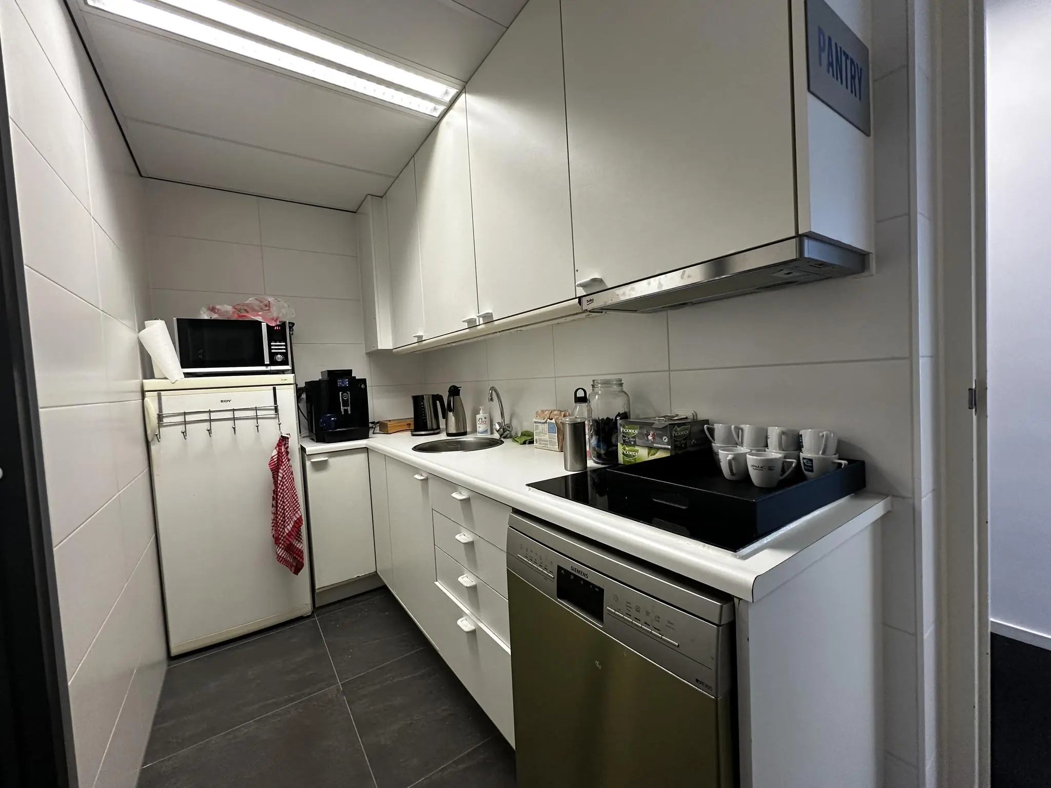 Kleine, witte bedrijfskeuken aan de Vreeswijksestraatweg met koffiezetapparaat, magnetron en servies.
