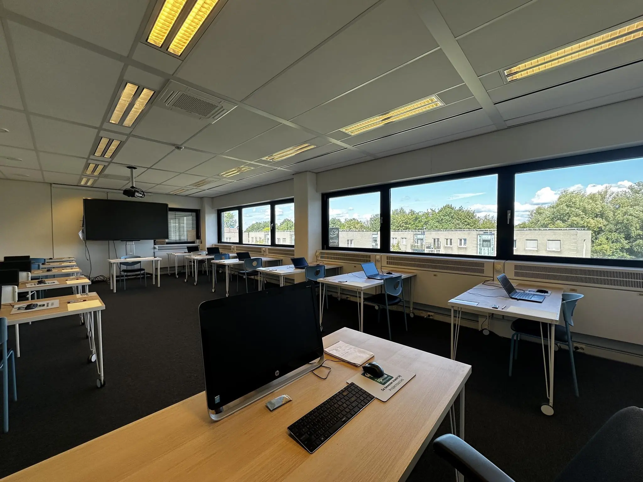 Lokaal aan de Vreeswijksestraatweg met meerdere werkplekken, computers en grote ramen met uitzicht op bomen en gebouwen.