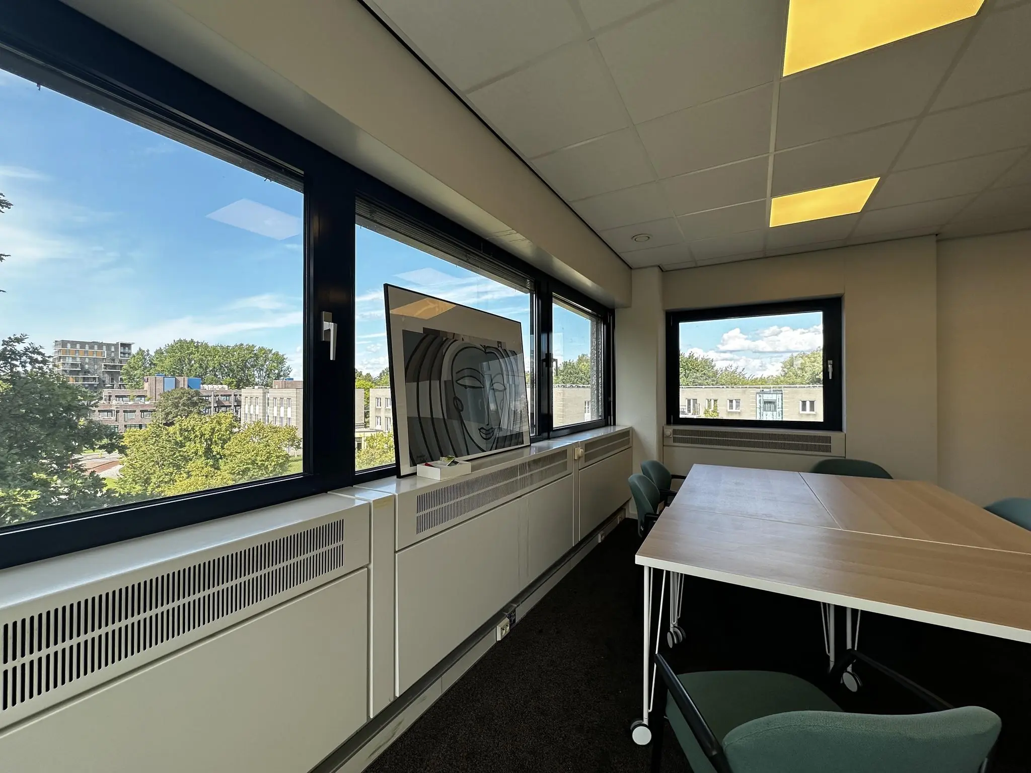Vergaderruimte aan de Vreeswijksestraatweg met grote ramen, een houten tafel en uitzicht op omliggende gebouwen en bomen.