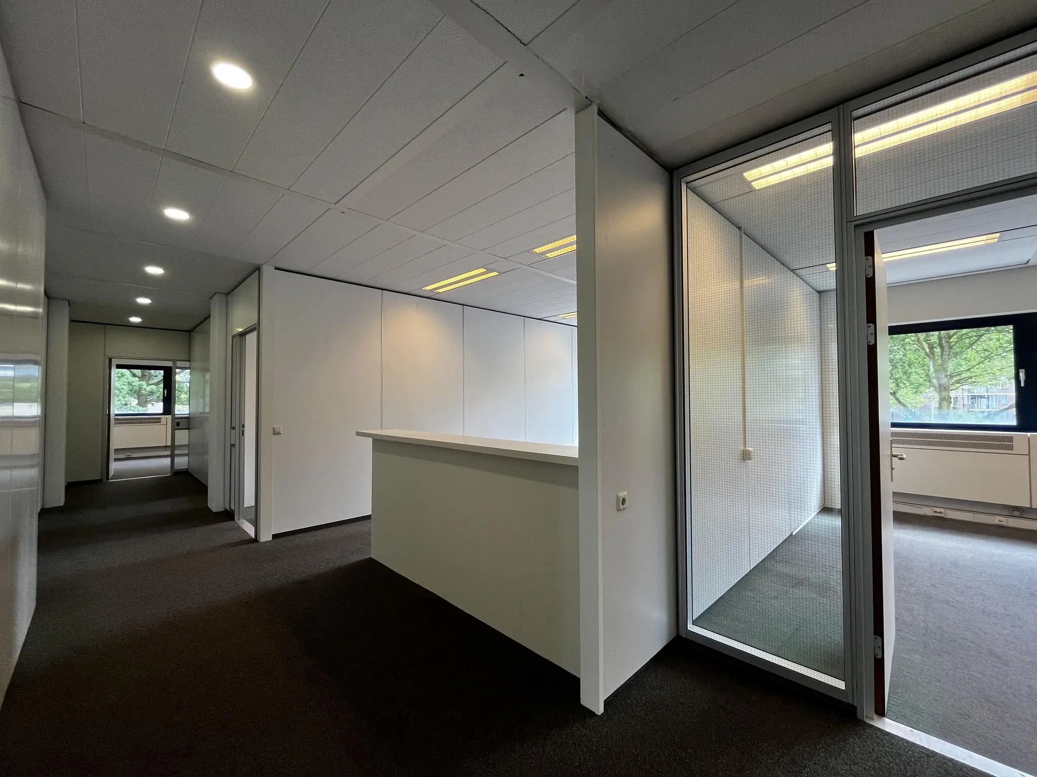 Modern kantoorinterieur aan de Vreeswijksestraatweg met strakke witte wanden, glazen kantoorruimtes en donker tapijt.