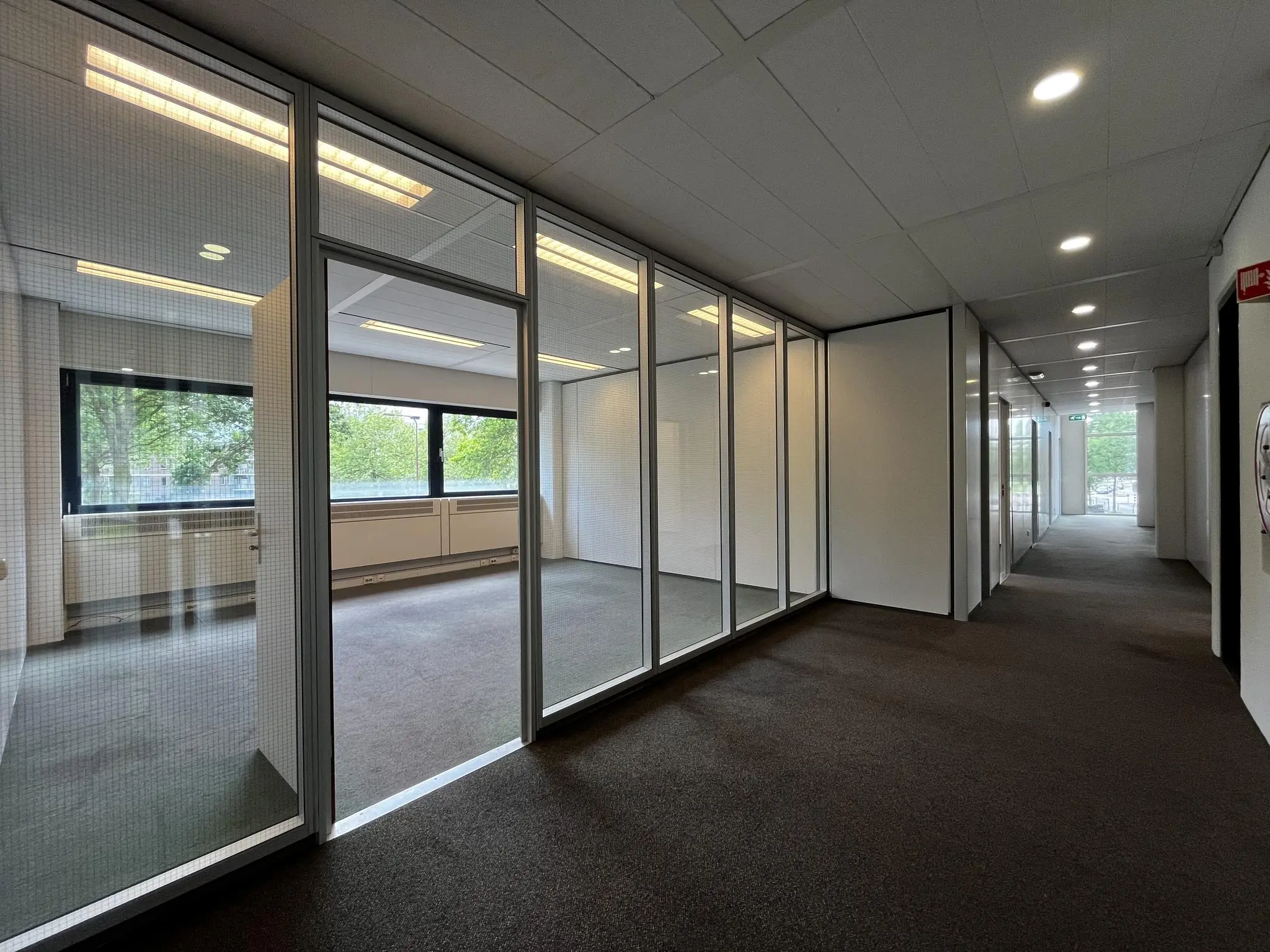 Gang met glazen wanden en uitzicht op een lege kantoorruimte aan de Vreeswijksestraatweg.