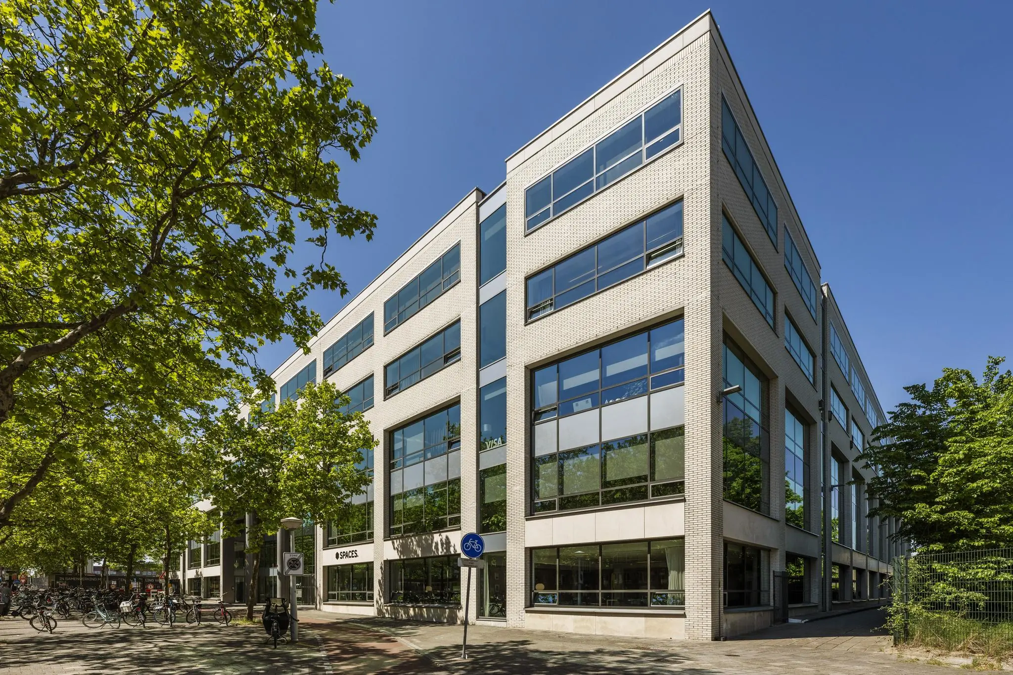 Modern kantoorgebouw aan de Mr. Treublaan in Amsterdam, omringd door bomen en fietsen.