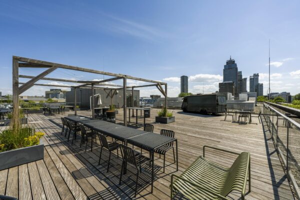 Dakterras aan de Mr. Treublaan met houten vlonder, zitplaatsen, plantenbakken en uitzicht op Amsterdamse kantoorgebouwen.