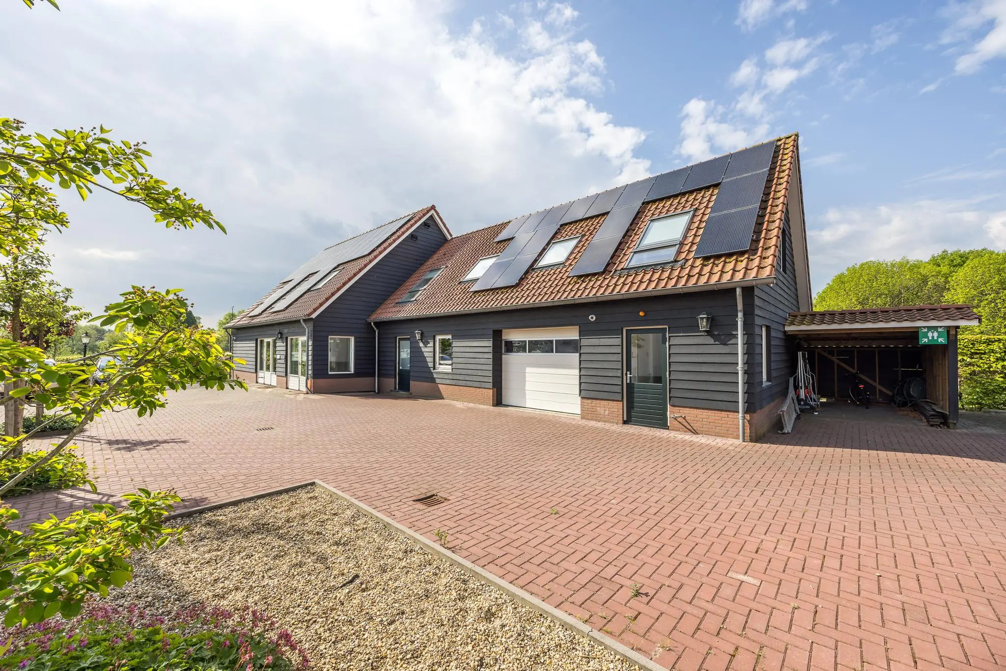 Moderne woning aan de Voorveste met zwarte gevelbekleding, zonnepanelen op het dak en een ruime oprit met carport.