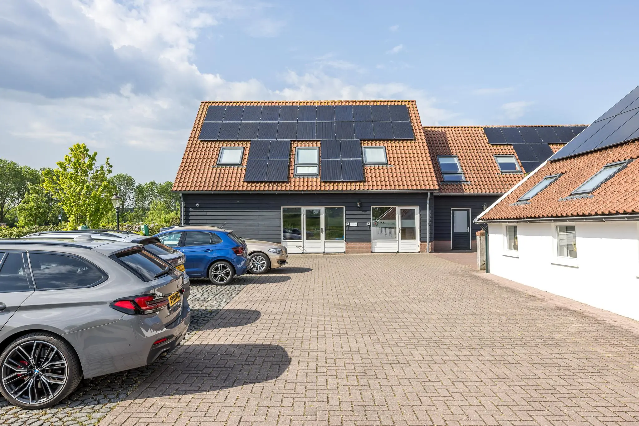 Een modern bedrijfsgebouw aan de Voorveste met zonnepanelen op het dak en geparkeerde auto's op de oprit.