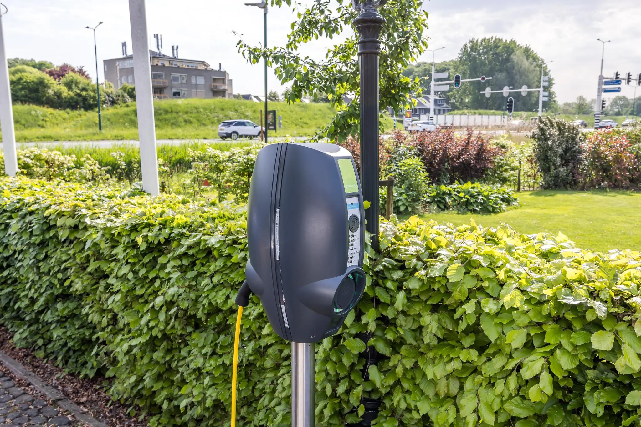 Laadpaal bij Voorveste omringd door groen en met verkeer op de achtergrond.