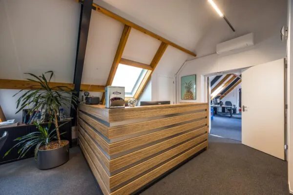 Moderne kantoorruimte op de Voorveste met houten receptiebalie, schuine plafonds en zicht op een werkruimte.