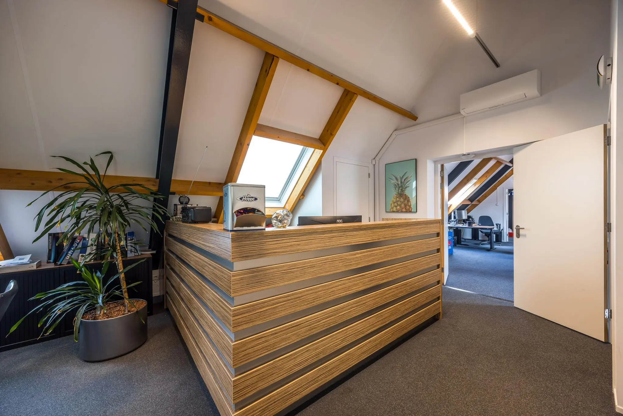 Moderne kantoorruimte op de Voorveste met houten receptiebalie, schuine plafonds en zicht op een werkruimte.