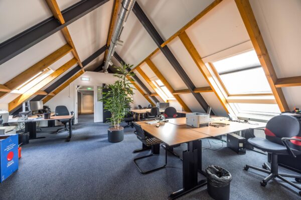 Zolderkantoor in Voorveste met schuine houten balken, meerdere bureaus en grote dakramen.