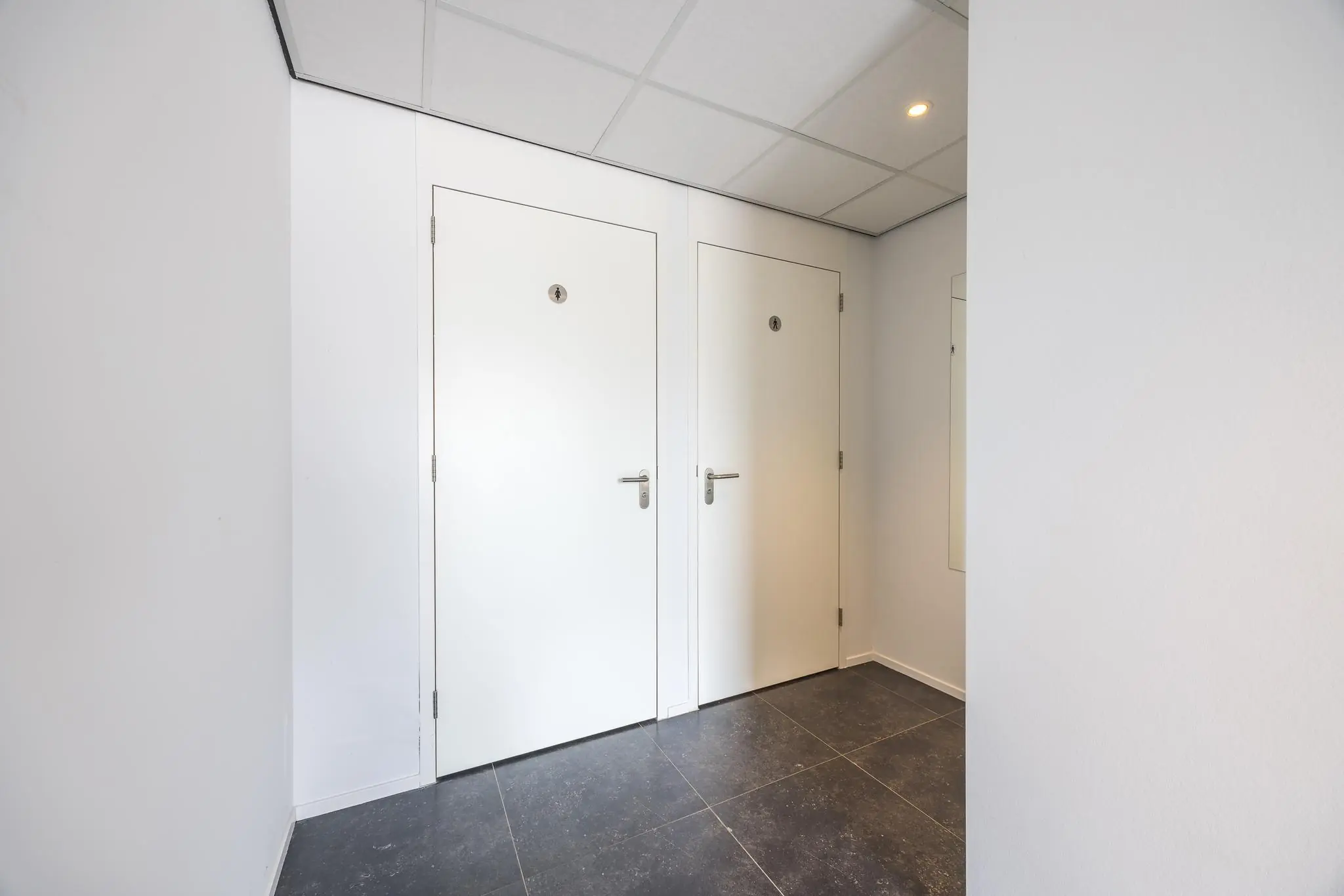 Twee witte toiletruimdeuren naast elkaar in een nette, modern afgewerkte gang in gebouw Voorveste.