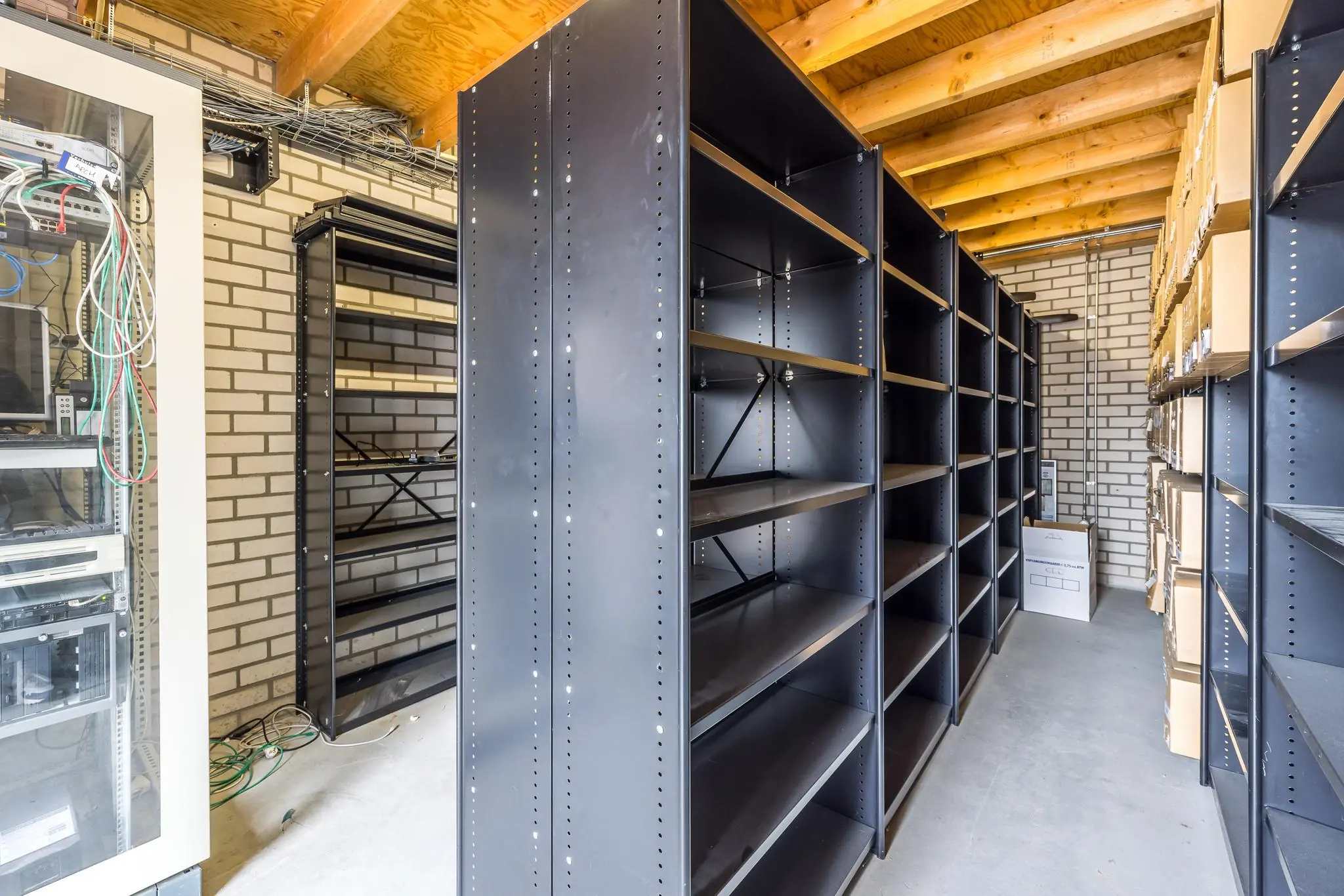 Opslagruimte met metalen stellingkasten en een netwerkkast in een gebouw aan de Voorveste.