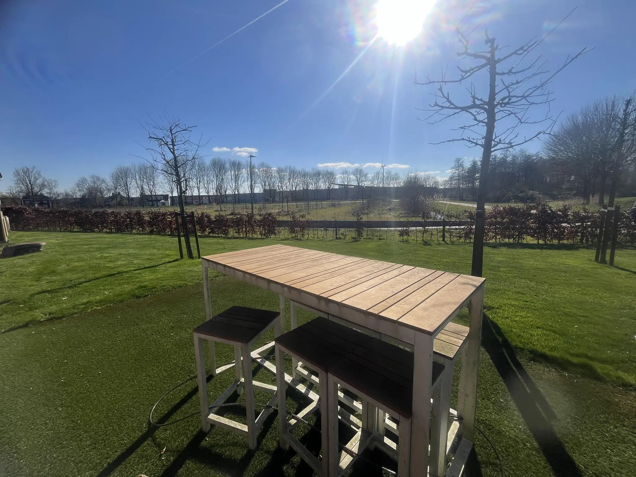 Houten tuintafel met krukken op een zonnige dag in een groene tuin bij Voorveste.