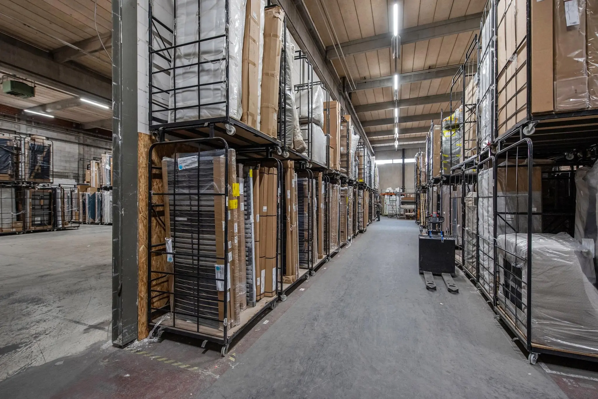 Gangpad in een magazijn aan de Limpergstraat met stellingen vol verpakte meubels en goederen op rolcontainers.