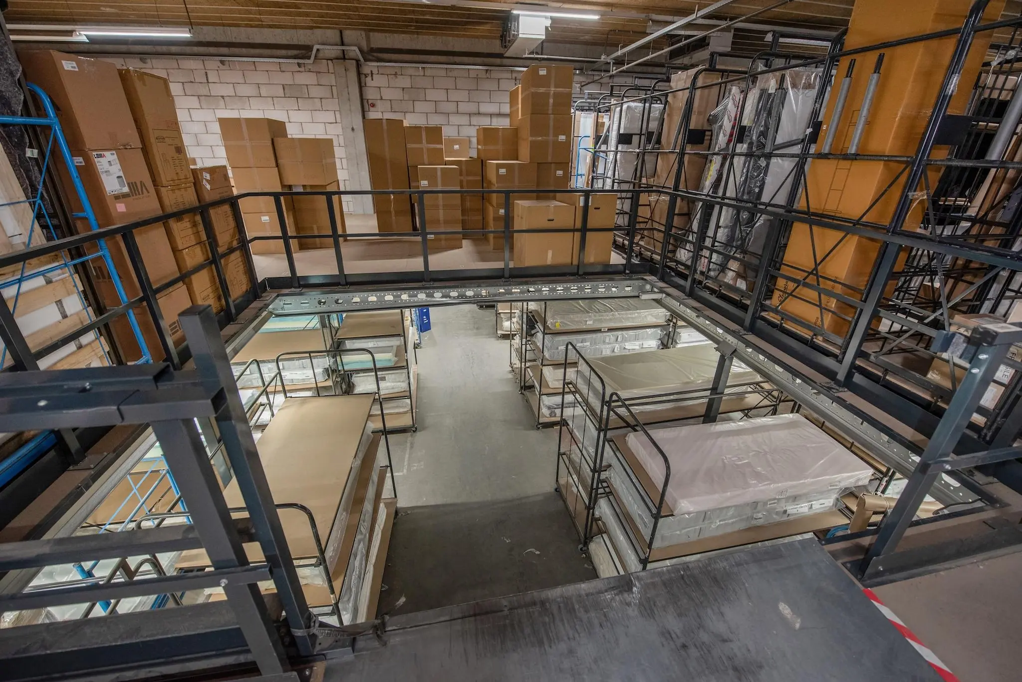 Magazijn aan de Limpergstraat met opgestapelde matrassen en kartonnen dozen op stalen stellingen.