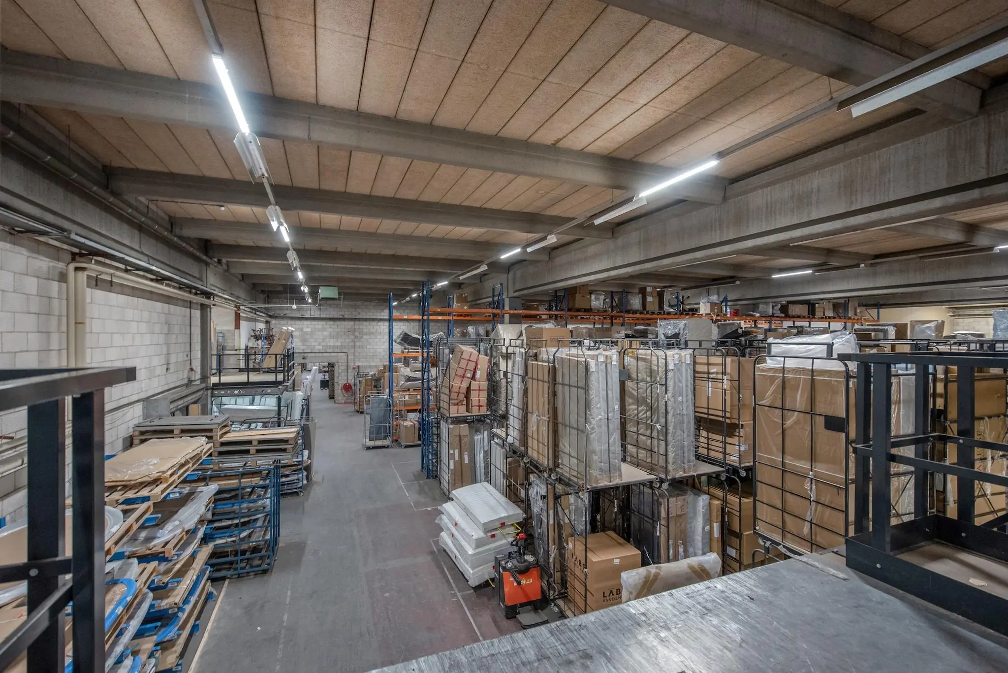Magazijn aan de Limpergstraat met metalen stellingen vol opgeslagen pallets, dozen en verpakte goederen.