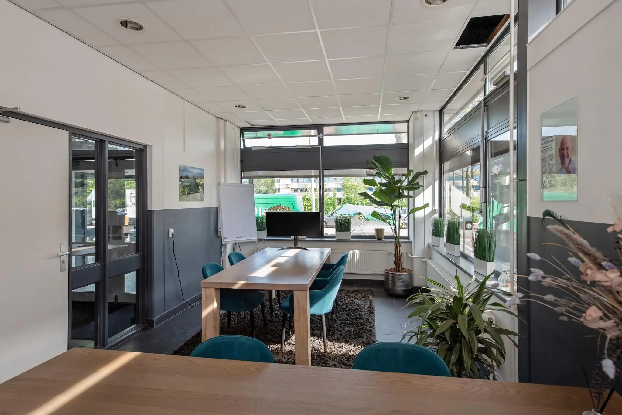 Moderne vergaderruimte aan de Limpergstraat met houten tafels, groene stoelen, veel planten en grote ramen met daglicht.