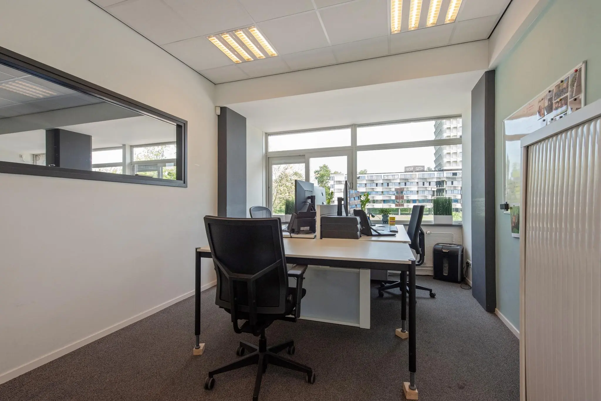 Modern ingericht kantoor aan de Limpergstraat met werkplekken, grote ramen en uitzicht op een appartementencomplex.