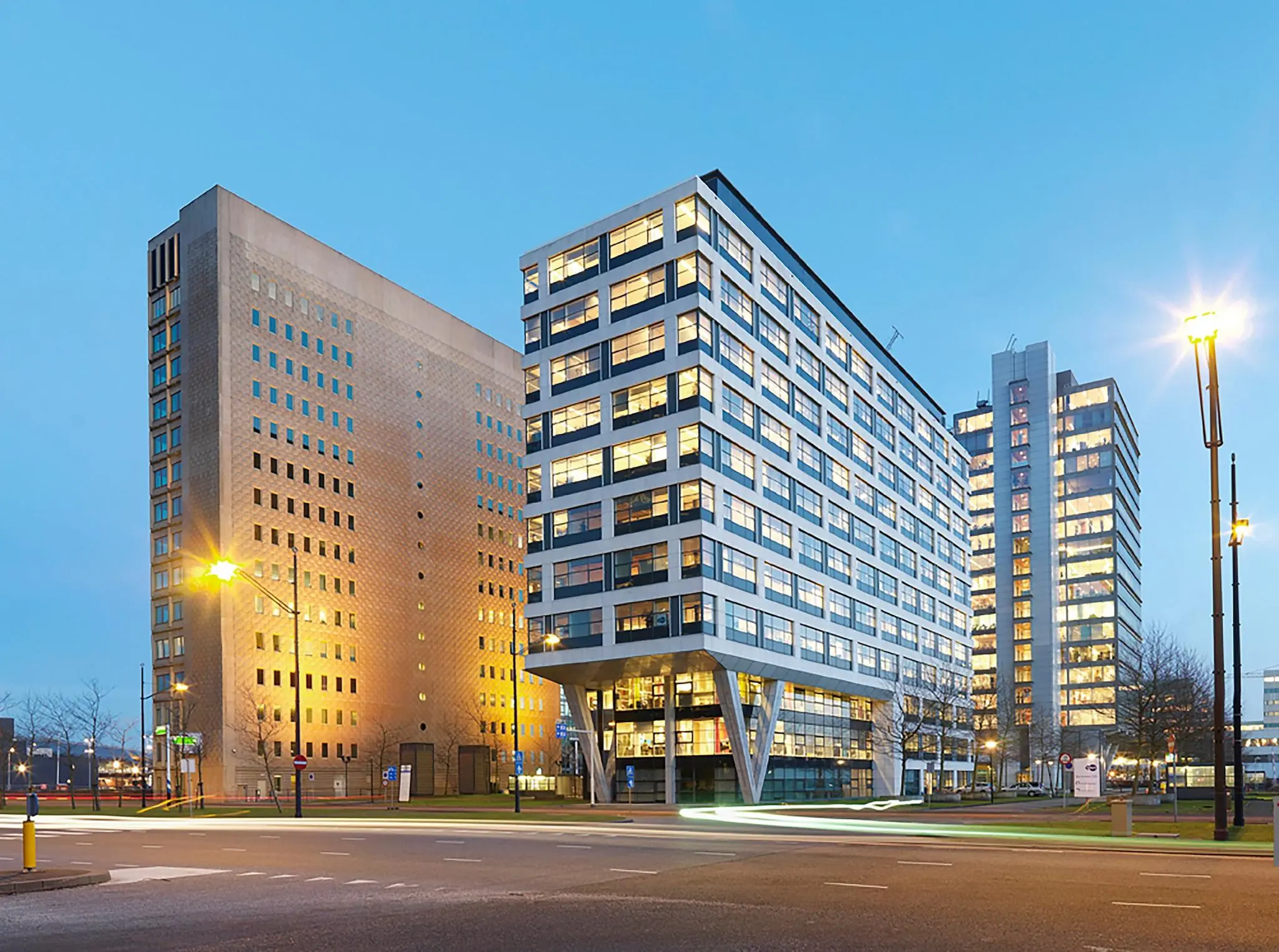 Kantoorgebouw De Entree in Amsterdam bij schemering, met verlichte ramen en een rustige straat op de voorgrond.