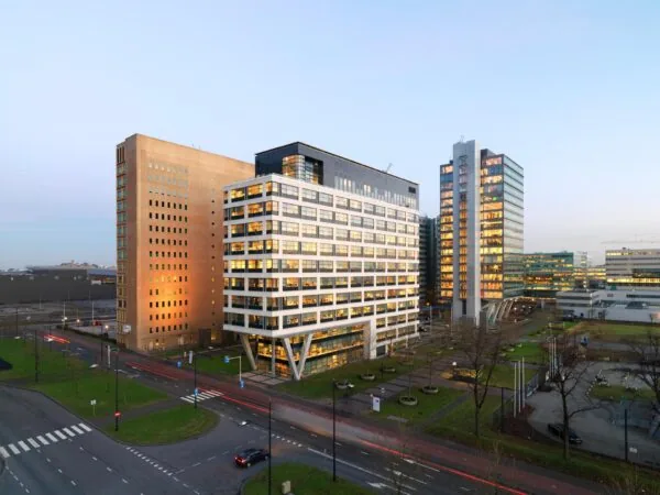 Kantoorcomplex De Entree in Amsterdam bij schemering, met verlichte ramen en omliggende wegen en groenvoorzieningen.