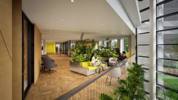 Moderne kantoorruimte De Entree met houten vloer, grote raampartijen, veel groen en mensen in gesprek op gele zitbanken.