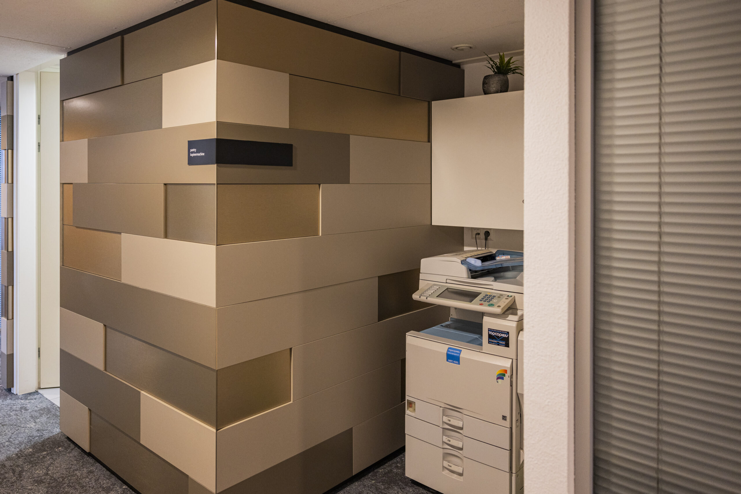 Een moderne kantoorruimte op de 23e etage met een kopieerapparaat en een geometrisch muurontwerp.
