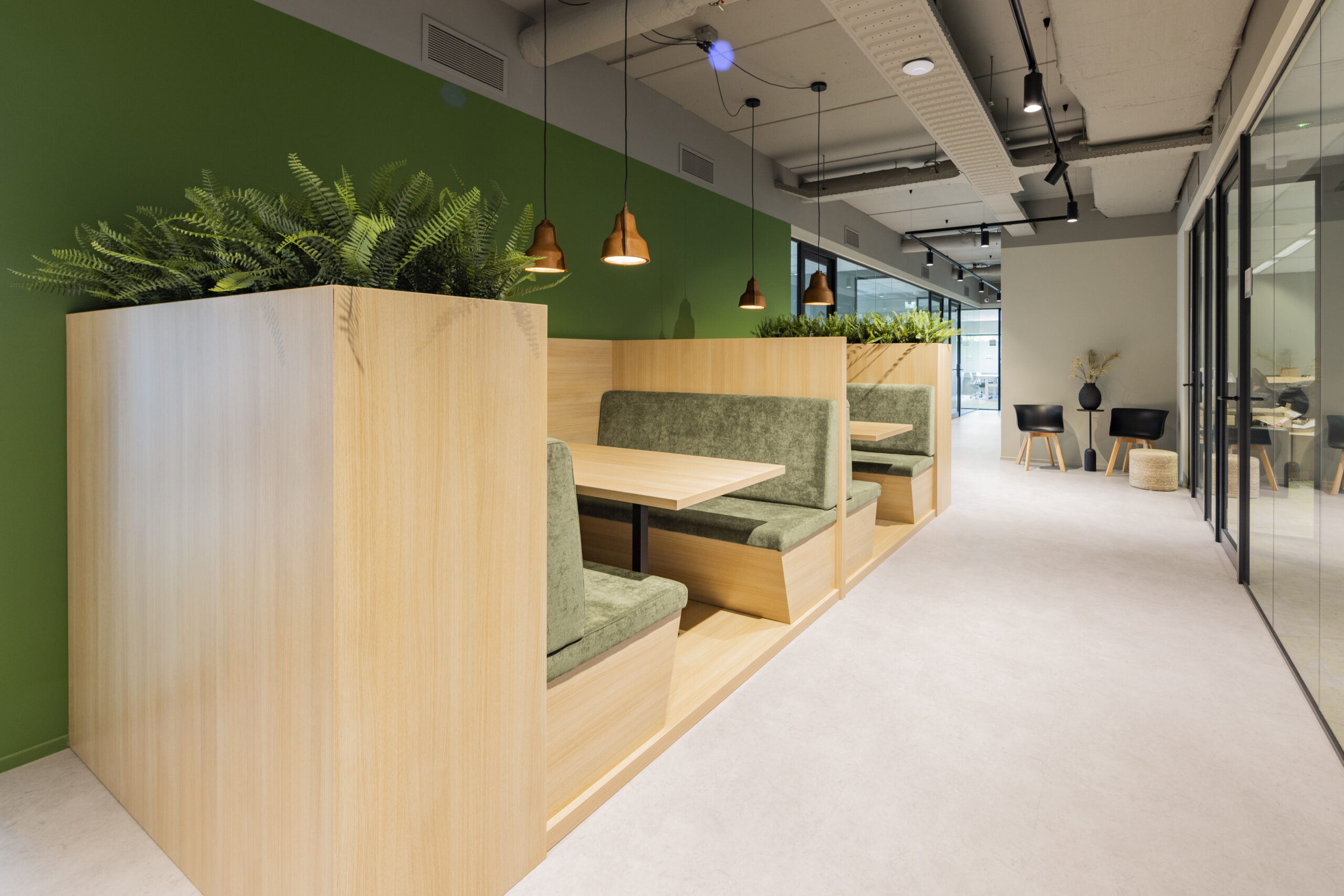 Een moderne kantoorruimte in Utrecht met houten zitbanken, groene bekleding en planten.