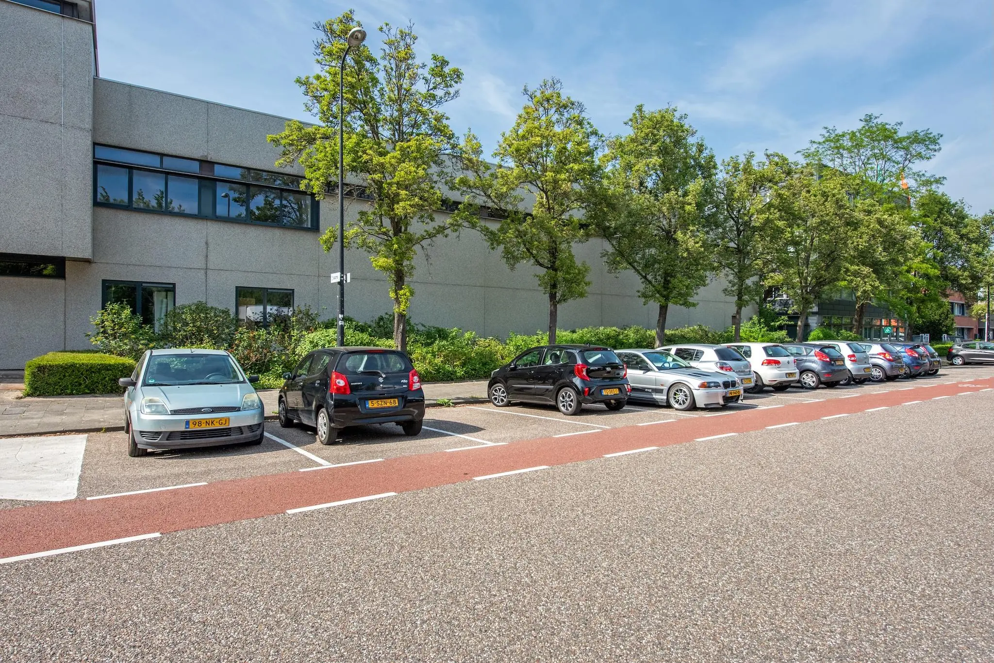 Rij geparkeerde auto’s langs de Limpergstraat voor een modern kantoorpand met bomen op de achtergrond.