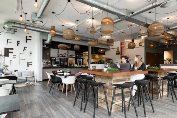 Modern ingerichte horecazaak aan de Fred. Roeskestraat met houten meubels, designverlichting en twee personen werkend op laptops aan een hoge tafel.