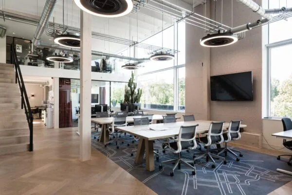 Moderne kantoorruimte aan de Fred. Roeskestraat met grote vergadertafels, bureaus, designverlichting en een hoge raampartij.