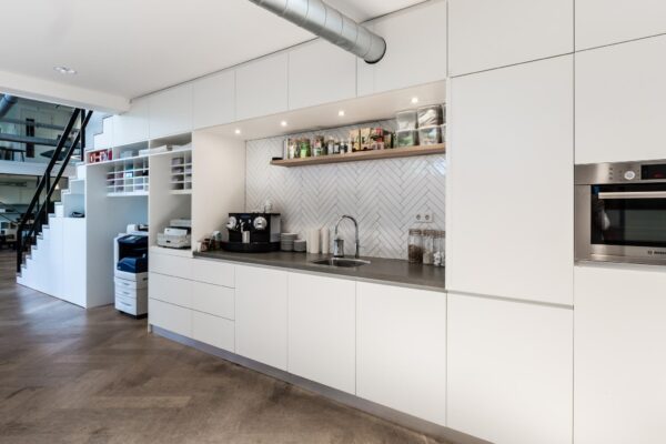 Moderne kantoorpantry aan de Fred. Roeskestraat met strakke witte kasten, ingebouwde apparatuur en een koffiehoek.