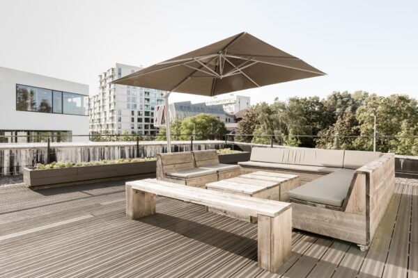 Dakterras aan de Fred. Roeskestraat met houten loungeset, parasol en uitzicht op omliggende moderne gebouwen.