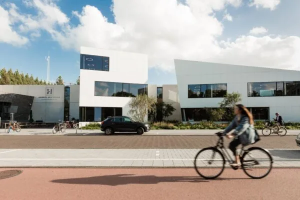 Voor het moderne witte kantoorgebouw aan de Fred. Roeskestraat in Amsterdam fietsen twee mensen op een zonnige dag voorbij.