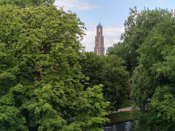 Uitzicht op de Domtoren in Utrecht, gezien vanaf de Maliesingel met veel groen en water op de voorgrond.