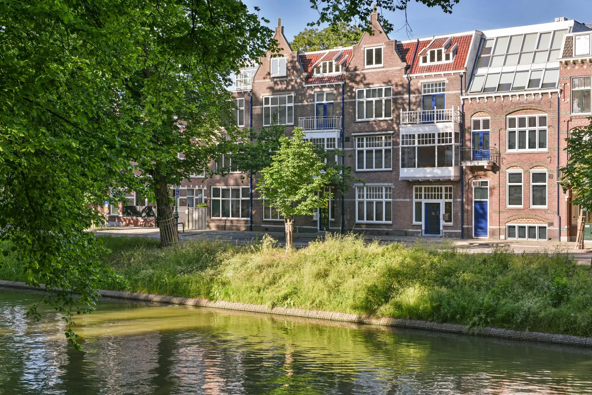 Rijtje karakteristieke herenhuizen aan de Maliesingel in Utrecht, gezien vanaf de overkant van de singel met bomen en water op de voorgrond.