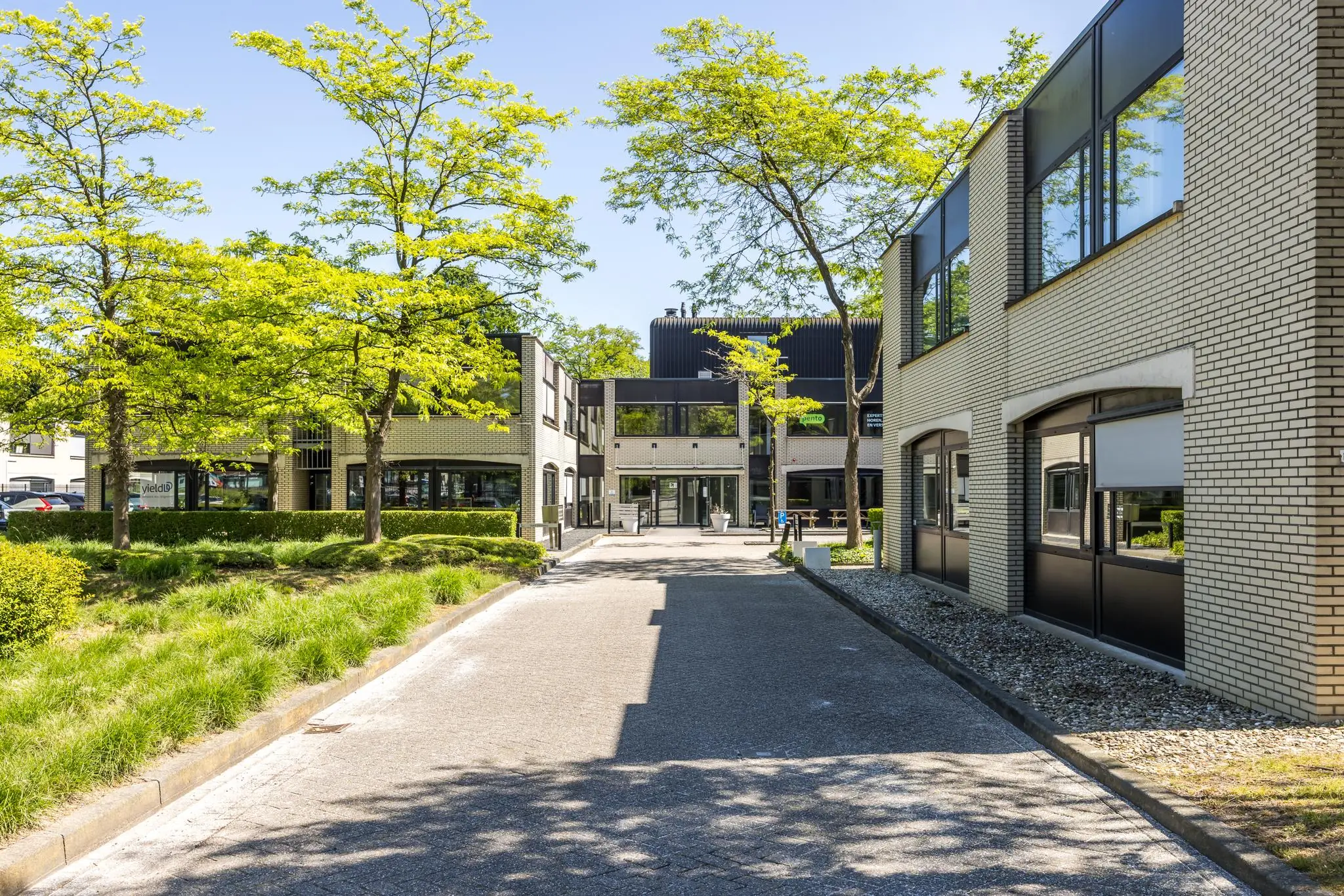 Moderne kantoorgebouwen aan de Burgemeester Verderlaan, omringd door groen en bomen op een zonnige dag.