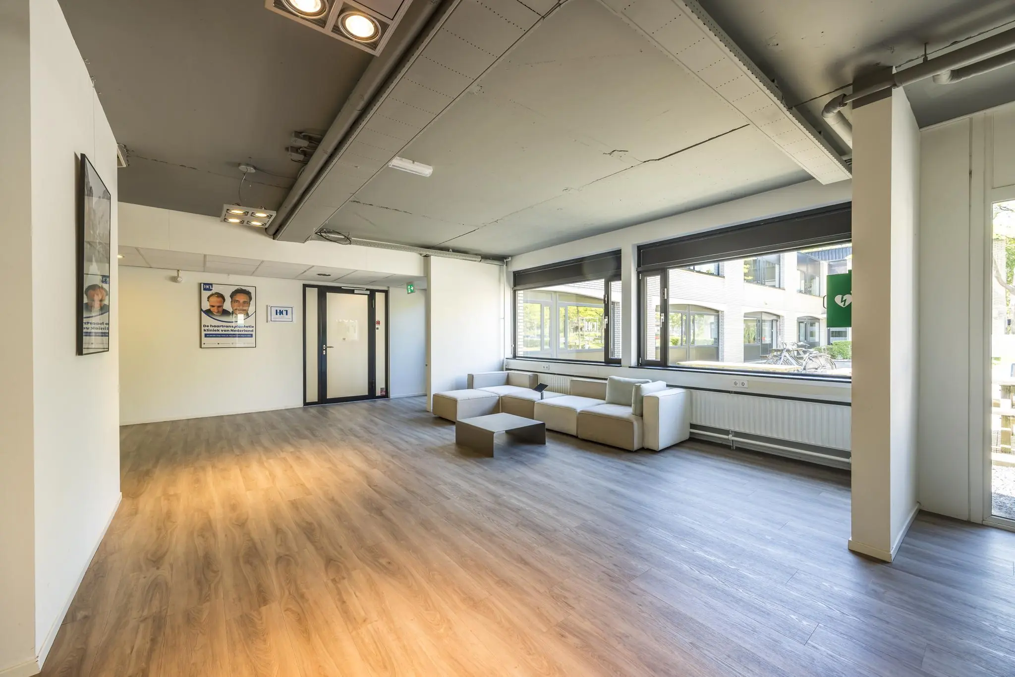 Moderne wachtruimte met lichte hoekbanken, houten vloer en grote ramen in het gebouw aan de Burgemeester Verderlaan.