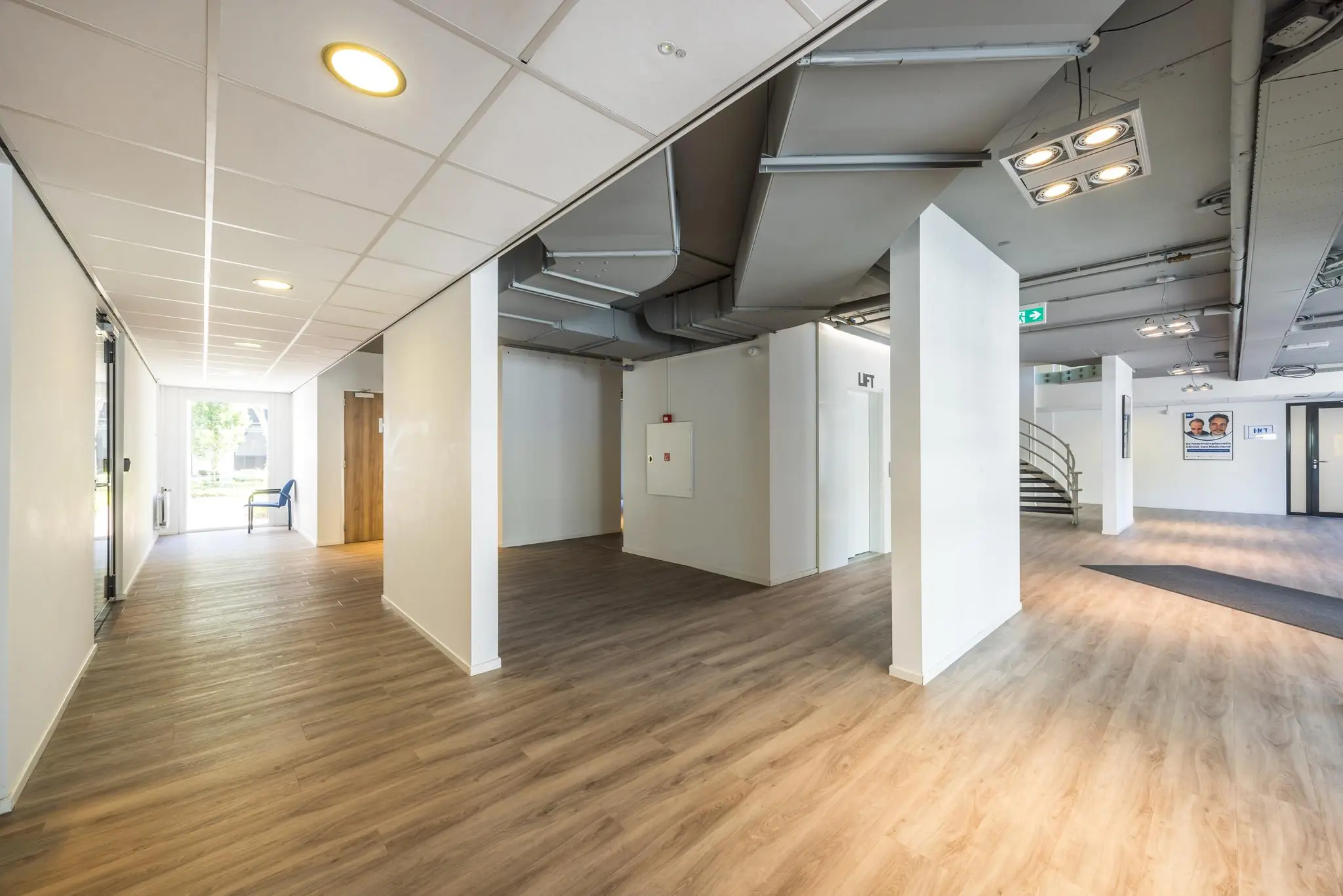 Lichte en moderne entreehal van een kantoorpand aan de Burgemeester Verderlaan met houten vloer, zichtbare ventilatiebuizen en een lift.
