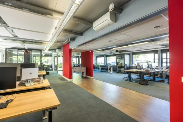 Modern kantoorpand aan de Burgemeester Verderlaan met open werkplekken, felrode zuilen en een tafelvoetbaltafel in het midden.