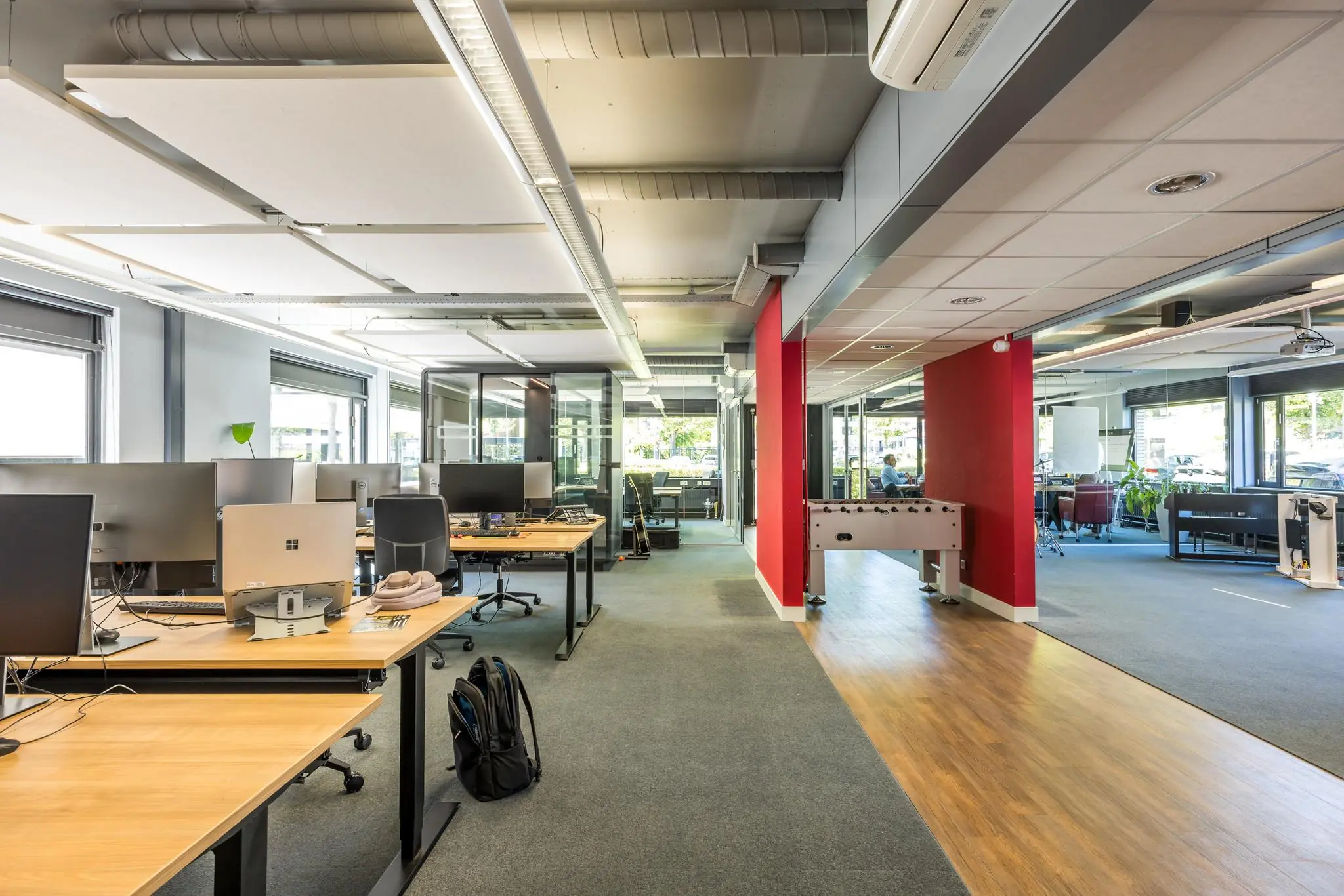 Modern kantoorinterieur aan de Burgemeester Verderlaan met werkplekken, glazen vergaderruimtes en een tafelvoetbaltafel.