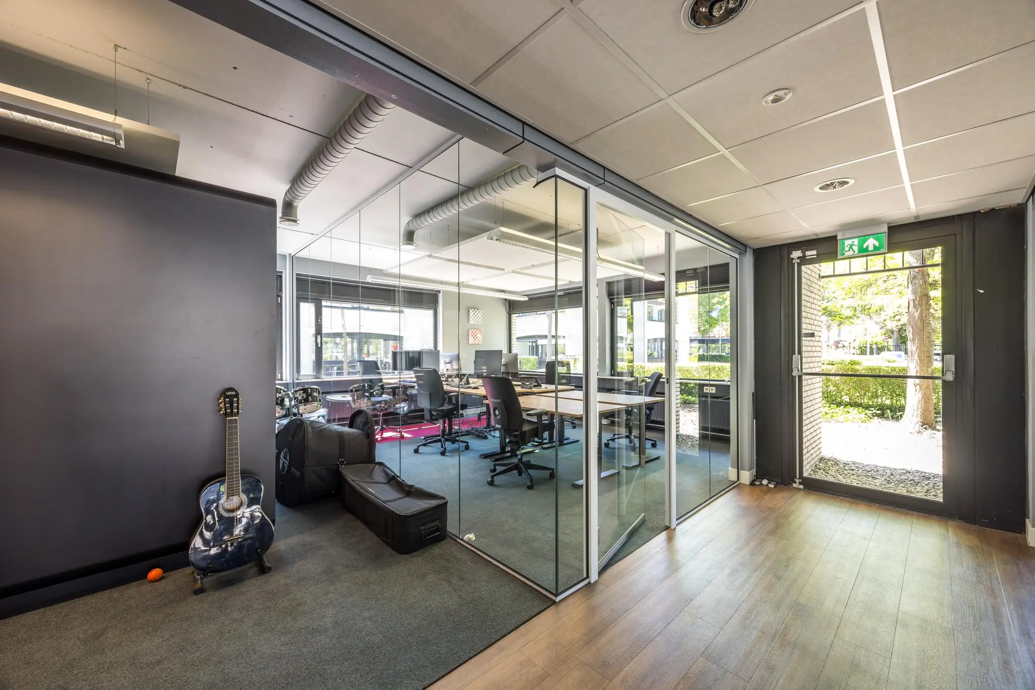 Moderne kantoorruimte aan de Burgemeester Verderlaan met glazen vergaderruimte, muziekinstrumenten en een open nooduitgang.